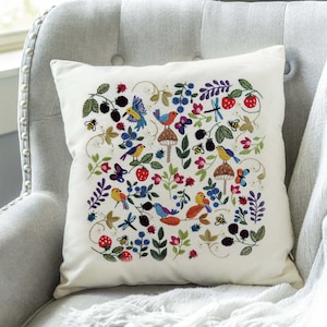 May include: A white cushion featuring a colourful embroidered design of birds, flowers, berries and insects. The design incorporates a range of colours, including red, blue, green, yellow and purple.