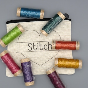 May include: A white canvas pouch with a heart and the word "Stitch" printed on it. The pouch is filled with eight spools of embroidery floss in various colours, including green, red, purple, blue, and orange.