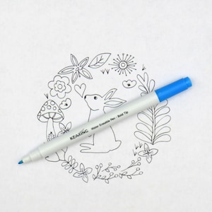 Puede incluir: Un bolígrafo blanco de tinta borrable con agua con una punta azul y el texto "KEARING Water Erasable Pen - Bold Tip" en el cuerpo. El bolígrafo está sobre una superficie blanca con un dibujo en blanco y negro de un conejo y flores.