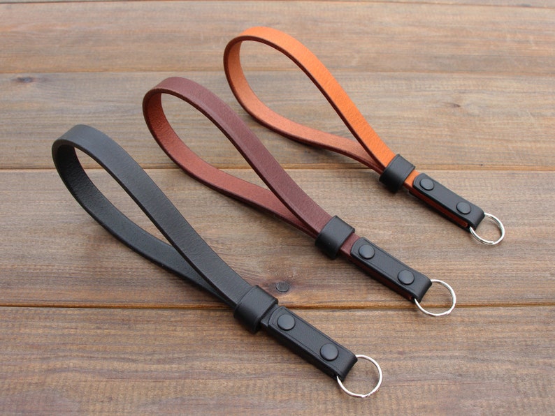 May include: Three leather keychains with metal rings. The keychains are black, brown, and orange.