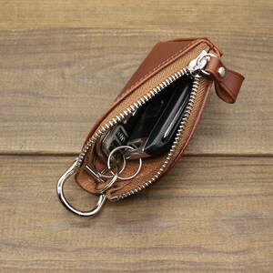 May include: A brown leather key holder with a zipper closure and a metal ring. The key holder is open and contains keys and a car key fob.