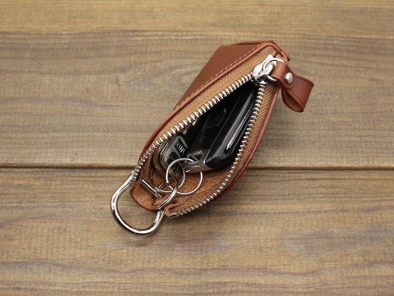 May include: A brown leather key holder with a zipper closure and a metal ring. The key holder is open and contains keys and a car key fob.
