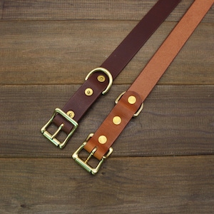 May include: Two leather dog collars with brass buckles and D-rings. The collars are brown and tan.