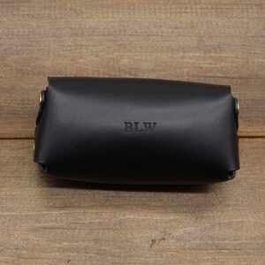 May include: A black leather case with brass hardware and the initials "BLW" embossed on the front.