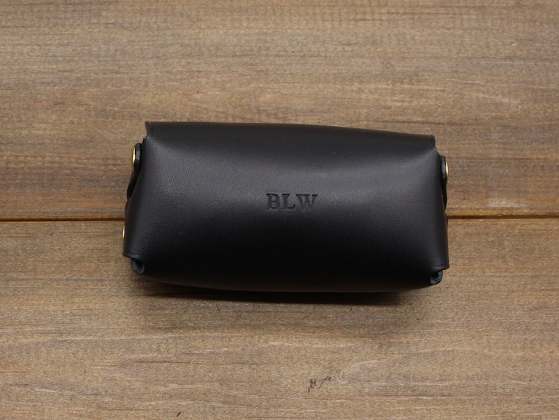 May include: A black leather case with brass hardware and the initials "BLW" embossed on the front.
