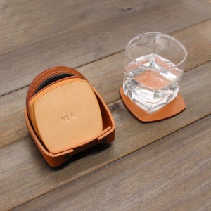 Puede incluir: Un juego de seis posavasos de cuero marr&oacute;n con un soporte de cuero. Los posavasos est&aacute;n apilados y el posavasos superior tiene las iniciales "BLW" grabadas.