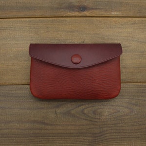 Puede incluir: Una peque&ntilde;a cartera de monedas de cuero rojo con cierre de bot&oacute;n.