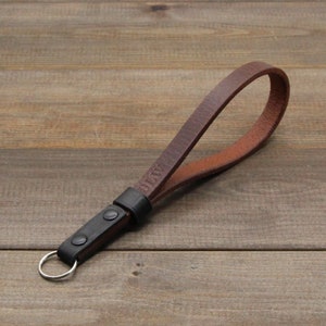 May include: A brown leather camera strap with a black leather loop and a silver key ring. The strap has the word "DIY" embossed on it.