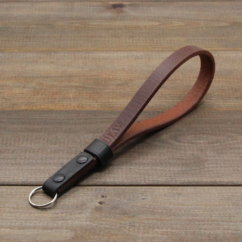 May include: A brown leather camera strap with a black leather loop and a silver key ring. The strap has the word "DIY" embossed on it.