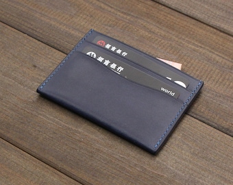 Può includere: Un porta carte in pelle blu scuro con un bordo cucito. Il porta carte ha tre slot per carte e la parola "world" è visibile su una delle carte.