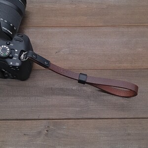 May include: A brown leather camera strap with black metal hardware. The strap has the initials "BLW" embossed on it.