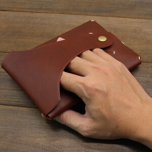 May include: A brown leather wallet with a flap closure and a white stitching detail. The wallet has a small brass button closure.