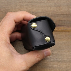 May include: A black leather case with gold accents. The case is closed and has a flap.