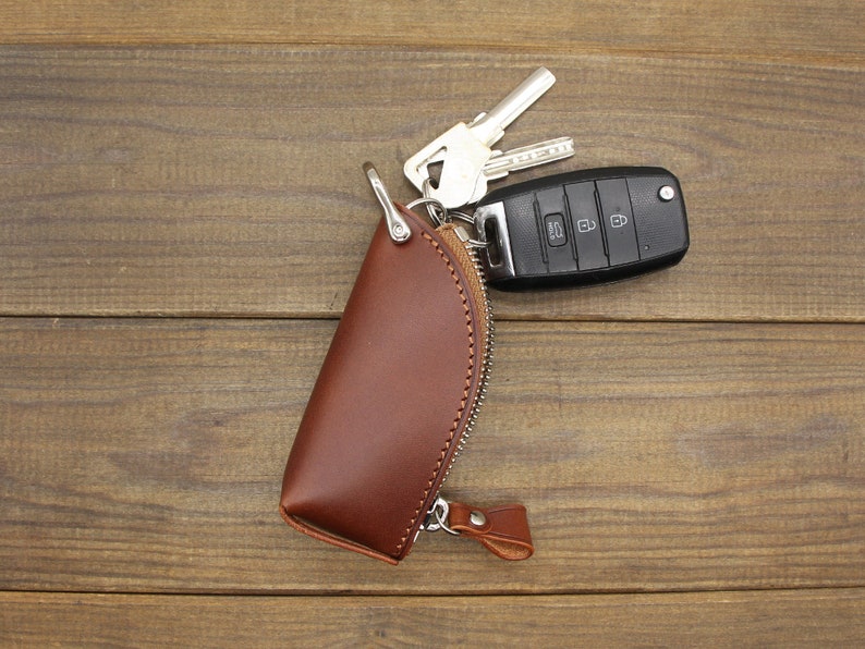 May include: A brown leather key holder shaped like a taco with a silver key ring and a car key attached.
