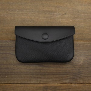 Puede incluir: Una cartera de monedas de cuero negro con cierre de presi&oacute;n.