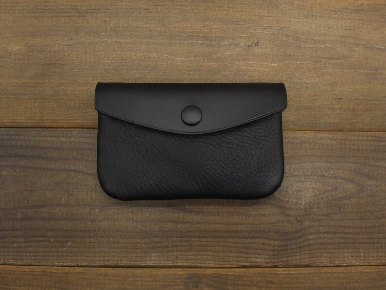 Puede incluir: Una cartera de monedas de cuero negro con cierre de presi&oacute;n.