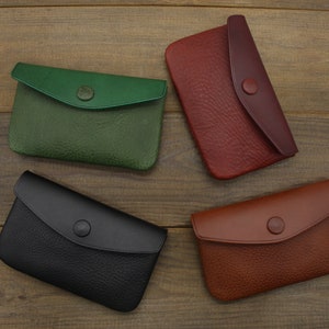 Puede incluir: Cuatro carteras de cuero en diferentes colores: verde, negro, rojo y marr&oacute;n. Cada cartera tiene una solapa con cierre de bot&oacute;n.
