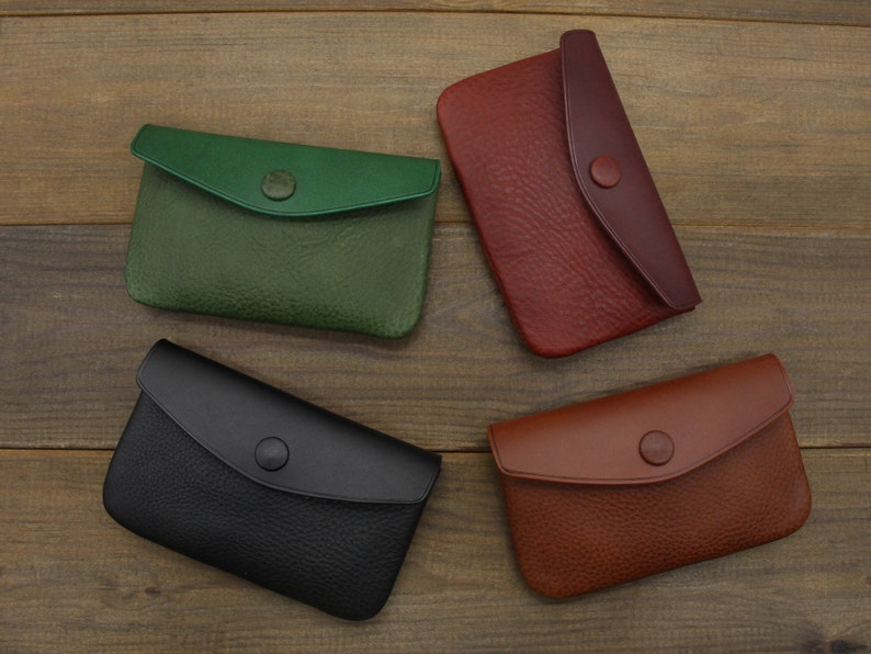 Puede incluir: Cuatro carteras de cuero en diferentes colores: verde, negro, rojo y marr&oacute;n. Cada cartera tiene una solapa con cierre de bot&oacute;n.
