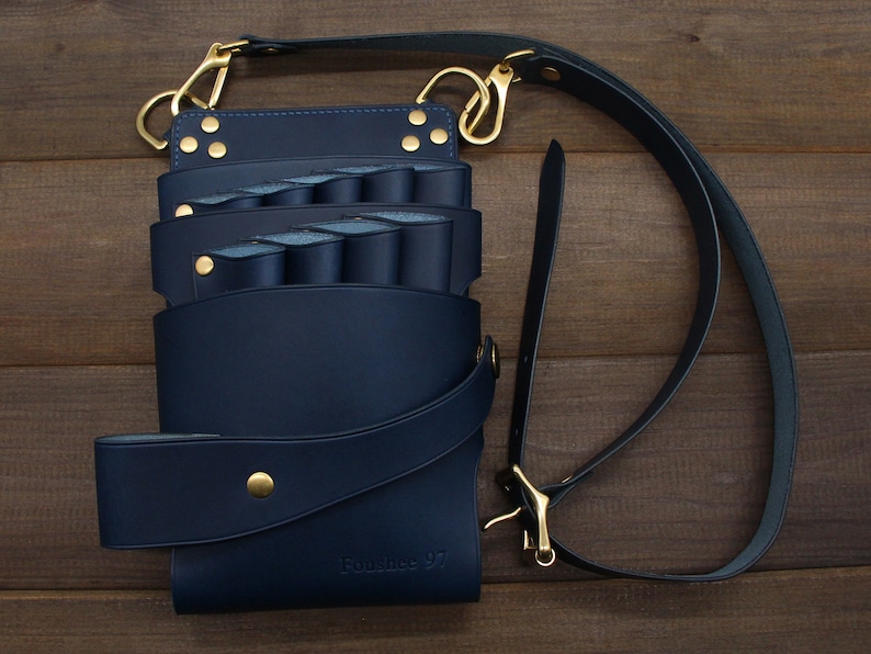 Puede incluir: Un organizador de herramientas de cuero azul marino con m&uacute;ltiples compartimentos y una correa para el hombro. El organizador tiene herrajes met&aacute;licos dorados, incluidos cierres y remaches. El texto "Fonshee 97" es visible en la parte delantera.