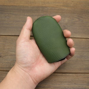 Puede incluir: Una bolsa de cuero verde oscuro con una textura lisa. La bolsa est&aacute; cerrada y tiene una costura alrededor del borde.
