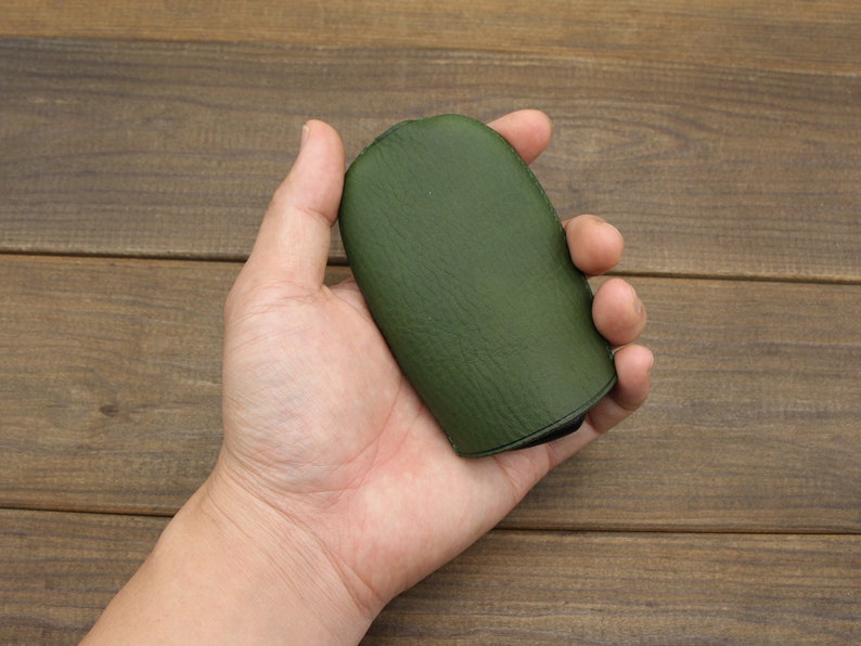 Puede incluir: Una bolsa de cuero verde oscuro con una textura lisa. La bolsa est&aacute; cerrada y tiene una costura alrededor del borde.