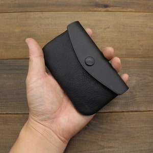 Puede incluir: Una peque&ntilde;a cartera de monedas de cuero negro con cierre de presi&oacute;n. La cartera es peque&ntilde;a y compacta, lo que la hace ideal para llevar efectivo o monedas.