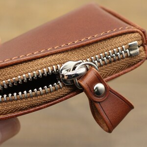 May include: A brown leather zippered wallet with a silver zipper pull. The wallet is closed and the zipper is pulled up.