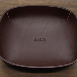 May include: A brown leather tray with a stitched edge and the date "6/26/19" embossed on the surface.