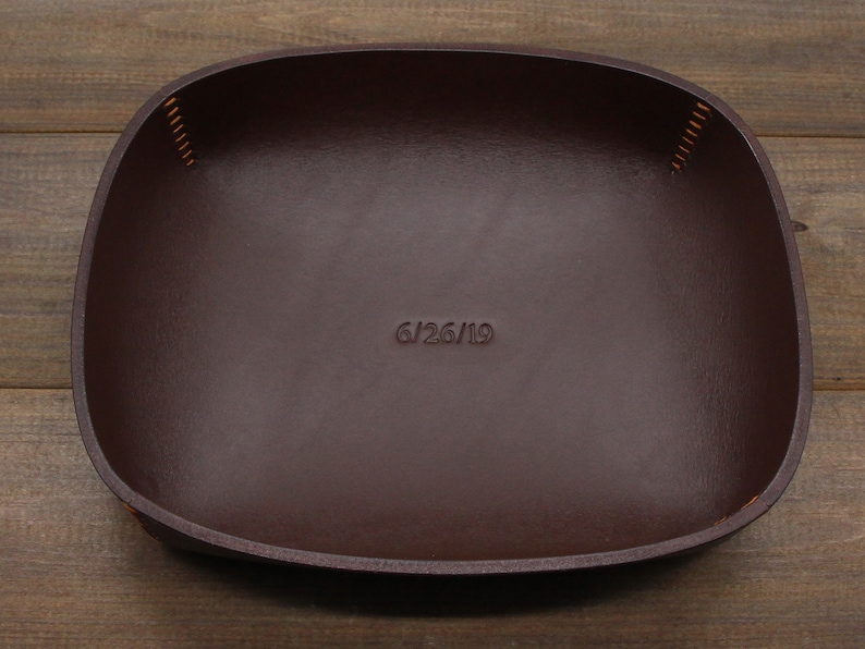 May include: A brown leather tray with a stitched edge and the date "6/26/19" embossed on the surface.