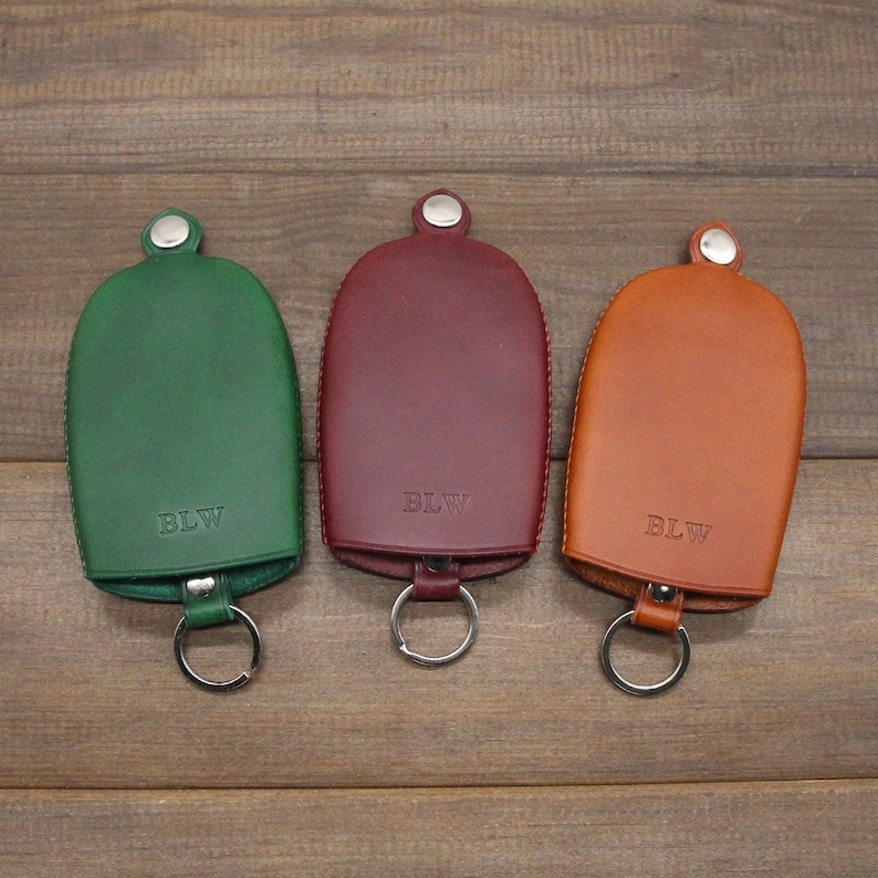 May include: Three leather key holders in green, burgundy, and tan. Each has a silver key ring and a snap closure. The initials "BLW" are embossed on each holder. The key holders are displayed on a wooden surface.