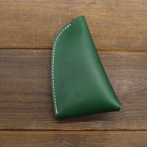 May include: A dark green leather coin purse with white stitching. The purse is shaped like a triangle and has a curved edge.