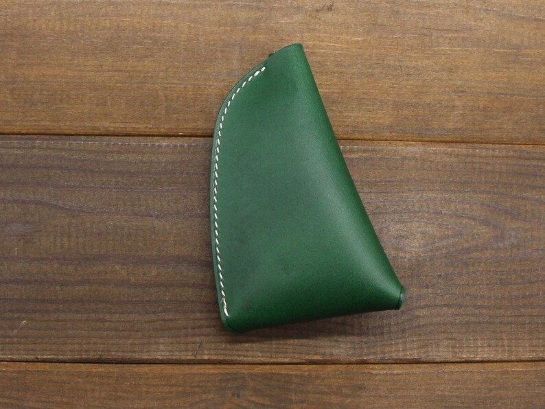 May include: A dark green leather coin purse with white stitching. The purse is shaped like a triangle and has a curved edge.