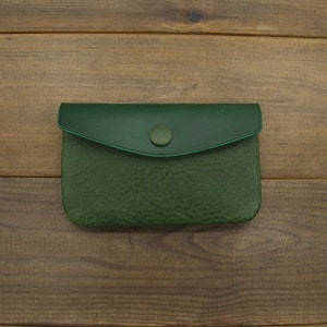 Puede incluir: Una peque&ntilde;a cartera de monedas de cuero verde con cierre de bot&oacute;n.