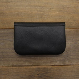 Puede incluir: Una cartera de monedas de cuero negro con cierre de solapa.