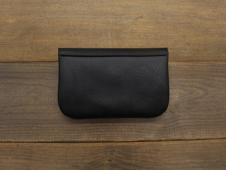 Puede incluir: Una cartera de monedas de cuero negro con cierre de solapa.