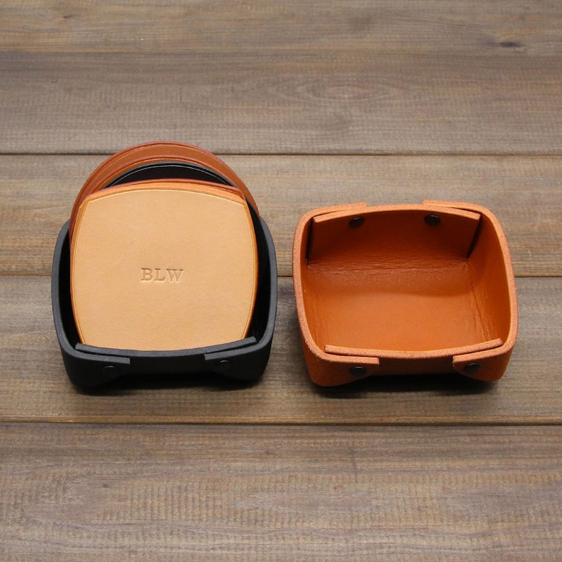Puede incluir: Dos bandejas de cuero, una con base negra y tapa de cuero marr&oacute;n con las iniciales "BLW" en relieve, y la otra una bandeja de cuero marr&oacute;n de forma cuadrada.