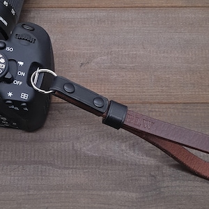 May include: A brown leather camera strap with black accents and the initials "BLW" embossed on the strap.