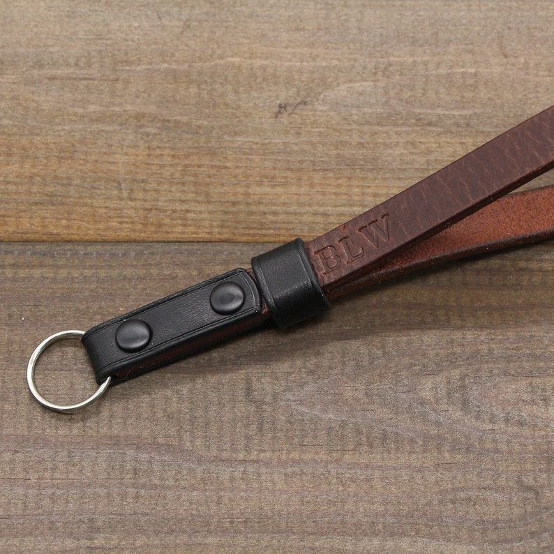 May include: A brown leather camera strap with a black leather adjustable strap and a metal ring. The strap is personalized with the initials "BLW".