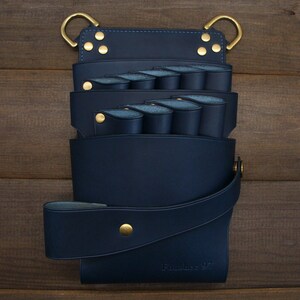 Puede incluir: Un cintur&oacute;n de herramientas de cuero azul marino con m&uacute;ltiples bolsillos y presillas, con herrajes de color lat&oacute;n. El cintur&oacute;n tiene una correa y est&aacute; dise&ntilde;ado para usarse alrededor de la cintura. El texto "Romance 97" es visible.