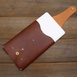 May include: A brown leather phone case with a white flap and a brown leather strap. The case has a gold button and white stitching.