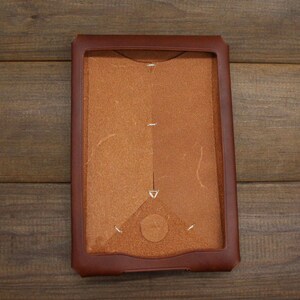 May include: A brown leather case with a flap closure. The case has a textured surface and is designed to hold a tablet or e-reader.
