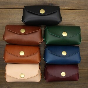 May include: Eight leather coin purses in different colors, including black, brown, green, blue, beige, and burgundy. Each purse has a gold button closure.