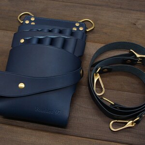 Puede incluir: Un cintur&oacute;n de herramientas de cuero azul marino con m&uacute;ltiples bolsillos y una correa para el hombro a juego. El cintur&oacute;n presenta herrajes dorados, incluyendo remaches, anillas en D y cierres. El texto "Foushee 97" est&aacute; grabado en la parte delantera.