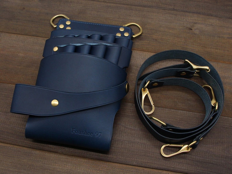 Puede incluir: Un cintur&oacute;n de herramientas de cuero azul marino con m&uacute;ltiples bolsillos y una correa para el hombro a juego. El cintur&oacute;n presenta herrajes dorados, incluyendo remaches, anillas en D y cierres. El texto "Foushee 97" est&aacute; grabado en la parte delantera.