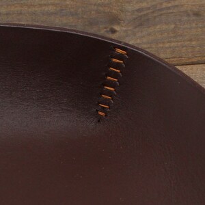 May include: Close-up of a brown leather tray with a stitched edge. The stitching is a light brown color.