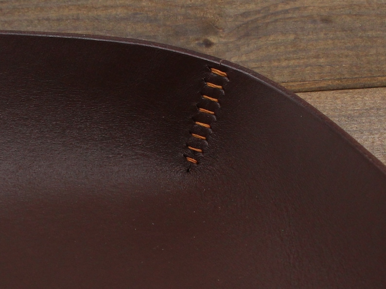 May include: Close-up of a brown leather tray with a stitched edge. The stitching is a light brown color.