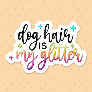 May include: A white sticker with the text "dog hair is my glitter" in black and rainbow colors. The sticker has a glittery effect and is on a peach background with a pattern of small triangles.