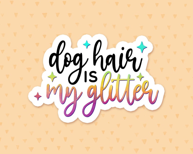 May include: A white sticker with the text "dog hair is my glitter" in black and rainbow colors. The sticker has a glittery effect and is on a peach background with a pattern of small triangles.