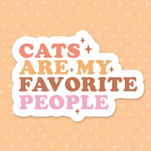 May include: A white sticker with the text "Cats are my favorite people" in colorful, retro-style lettering. The text is in pink, orange, yellow, and brown. There are small stars around the text.