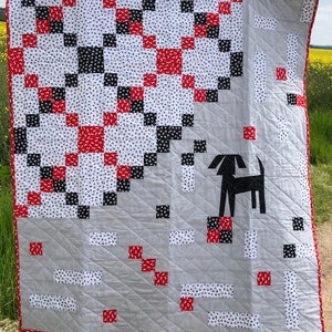 May include: A quilt with a black and white checkered pattern and red accents. The quilt is made up of squares and has a dog silhouette in the lower right corner.
